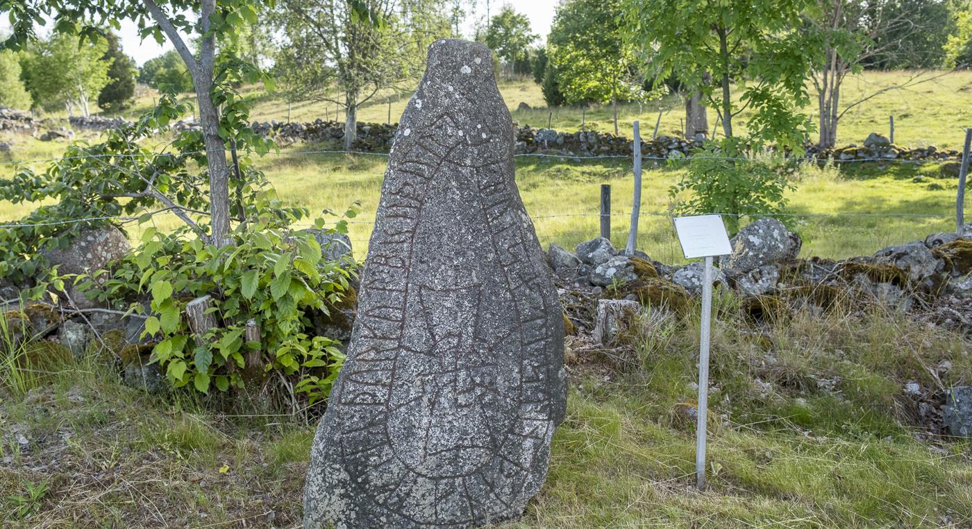 En stor runsten som står framför en stenmur mitt på ett fält.