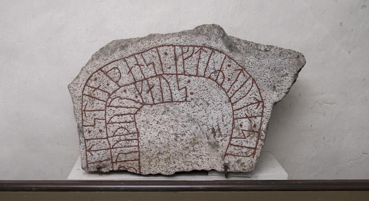 En runsten med skrift i rött mot en vit bakgrund.