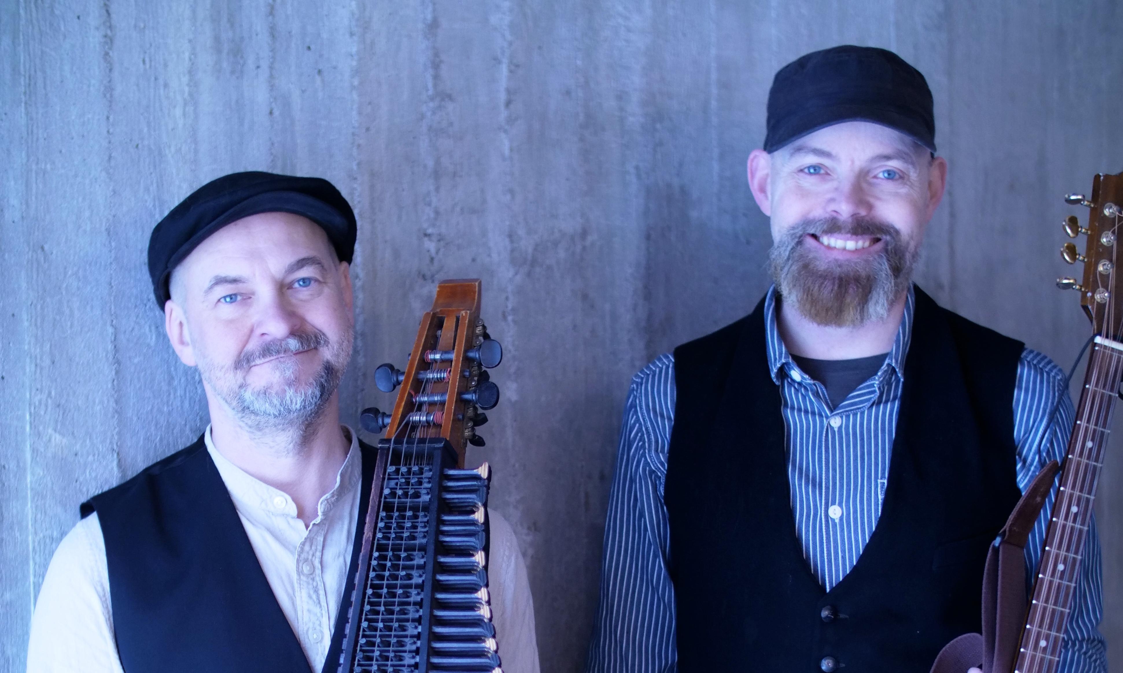 Två män som håller nyckelharpa respektive annat stränginstrument i handen