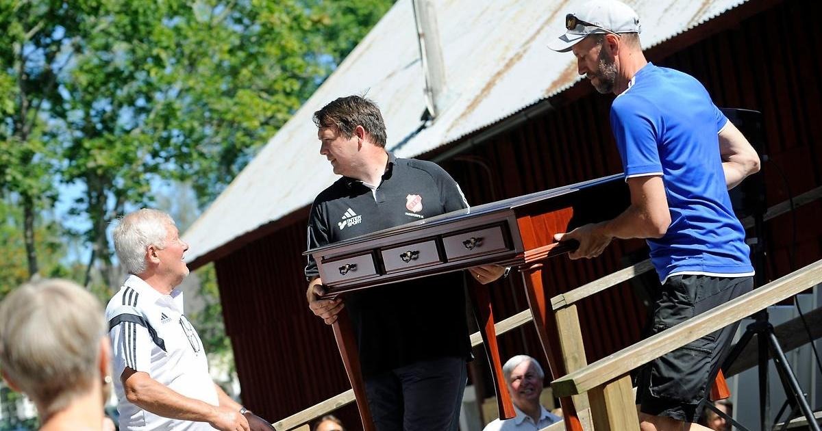 Två män bär ut ett vackert skrivbord från auktionslokalen