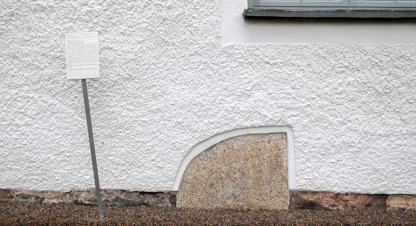 En vit byggnad med en runsten framför sig.