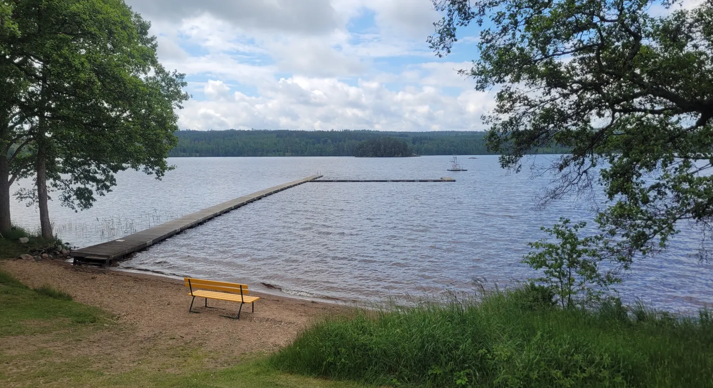 En bänk som står vid stranden av Klockesjöbadet.