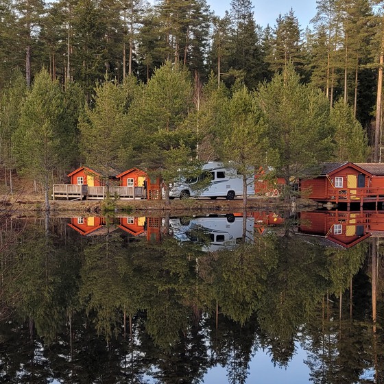 Smålandsfiskarna, en husbil står parkerad intill en sjö och en stugby.