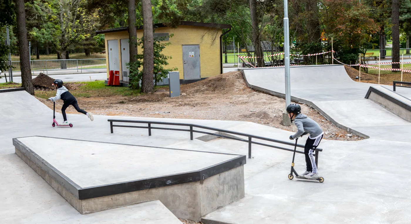 Två barn som åker kickbike i en skatepark.