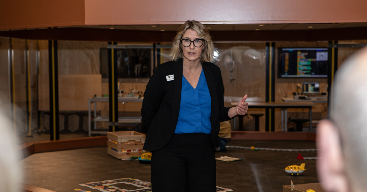 En kvinna står framför en liten scen och presenterar.