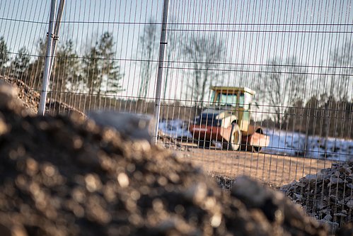 En inhägnad byggarbetsplats. Innanför inhägnaden syns en maskin.